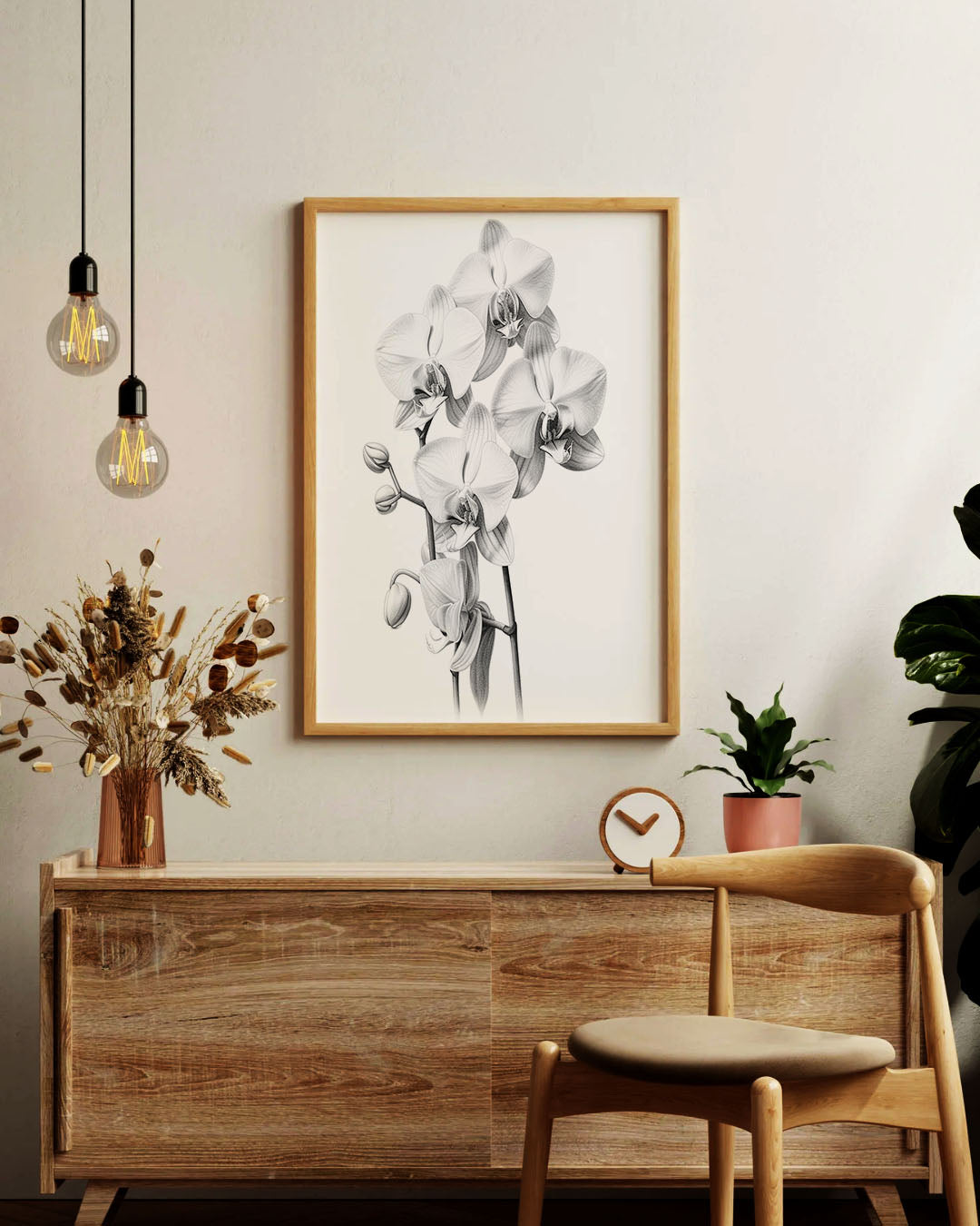 A framed black and white botanical art print of orchids hanging on a light beige wall above a wooden console table in a styled room setting.